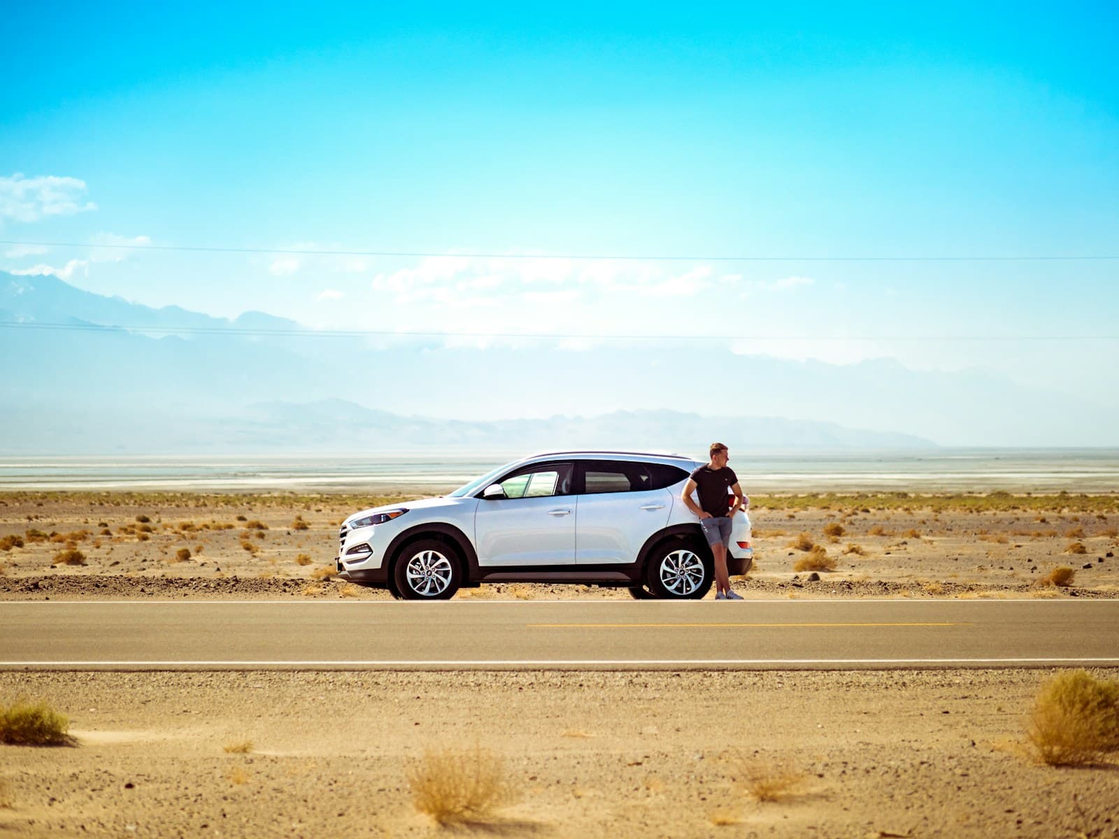 White SUV parked on a desert road with a person standing beside it below mountains